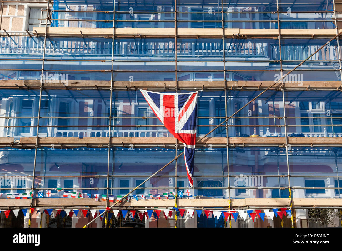 Periodo grande edificio in fase di ristrutturazione con ampia impalcatura e drappeggiati in una rete di protezione, bunting e bandiera europea. Foto Stock