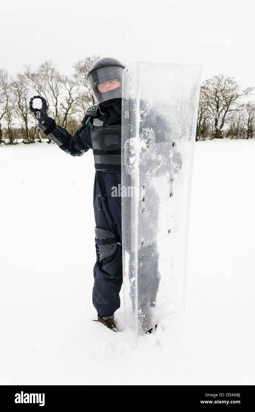 Funzionario di polizia vestito in tenuta da sommossa in procinto di lanciare una palla di neve Foto Stock