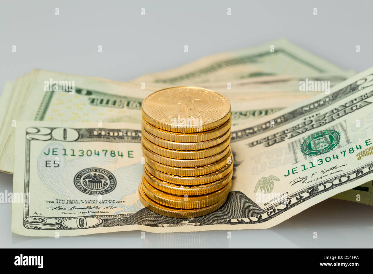 Le monete d'oro in piedi su molti $20 fatture del dollaro e le note sul tavolo bianco Foto Stock