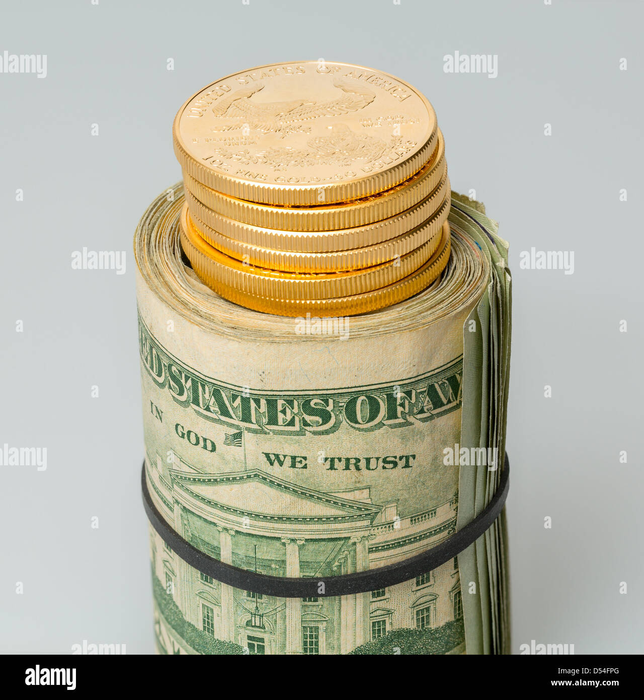 Le monete d'oro in piedi sul rotolo di molti $20 fatture del dollaro e note fissato dalla fascia elastica sul tavolo bianco Foto Stock