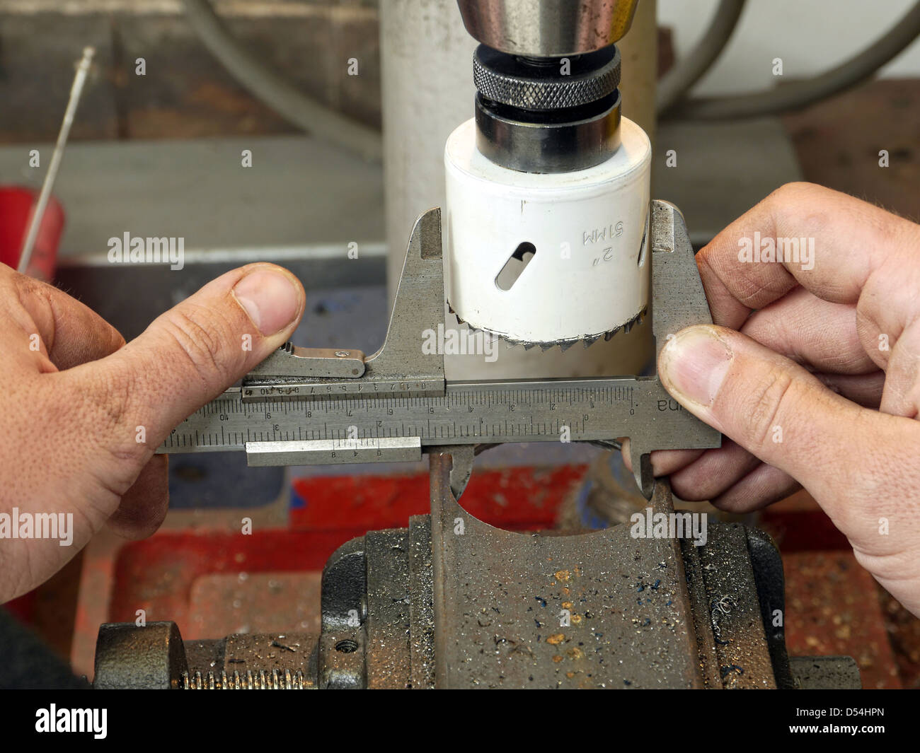 Vista dettagliata del macchinista lavoratore mani prendendo una misurazione del diametro del foro ricavato in un pezzo di metallo utilizzando pinza Foto Stock