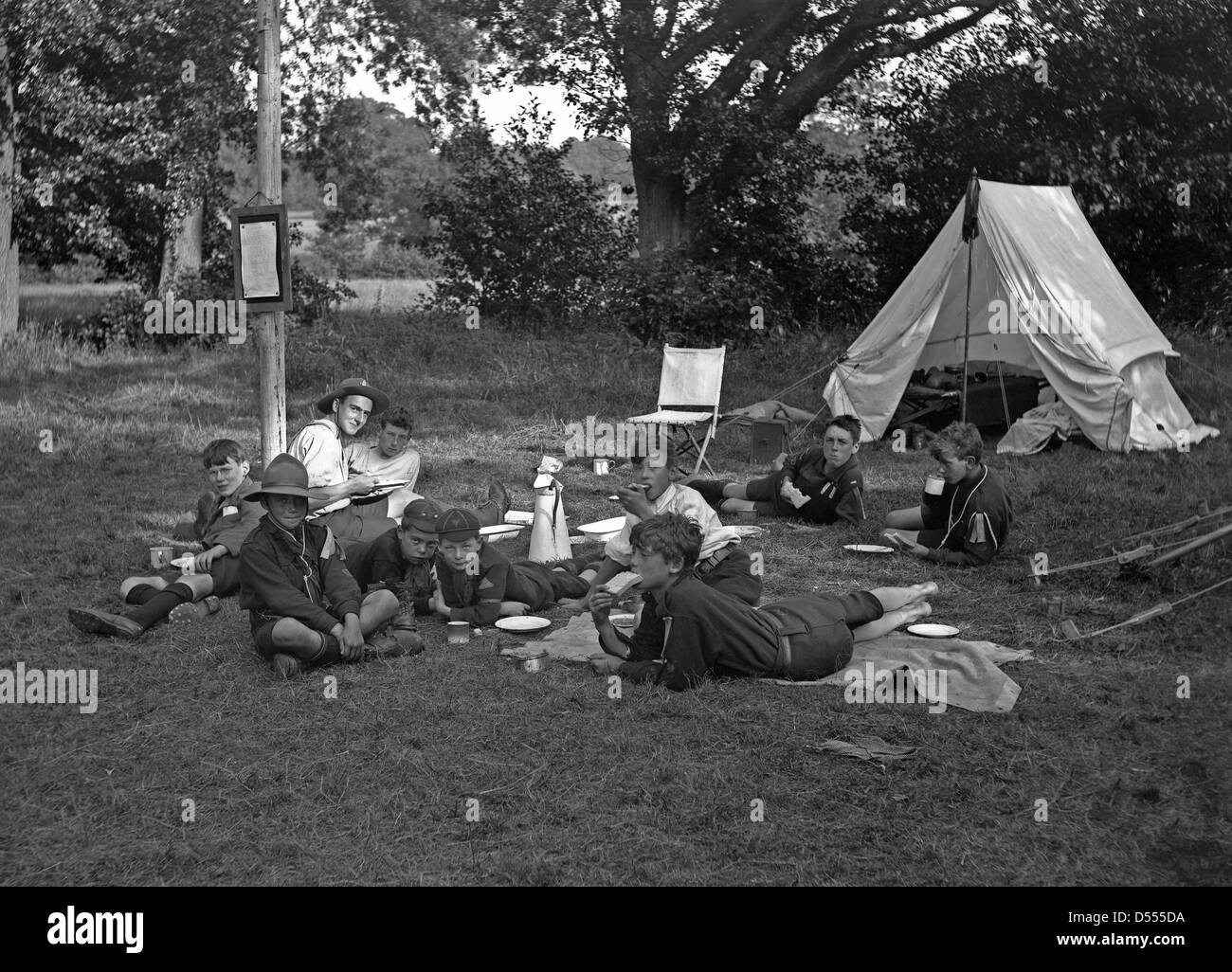 Boy Scout camp, c. 1930 con la tenda e la piantò gli scout e scout master mangiando panini Foto Stock