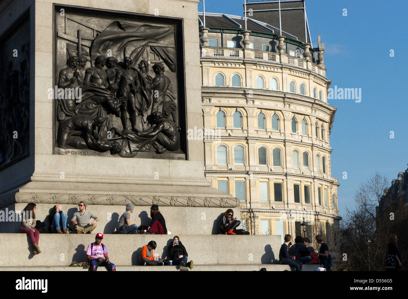 Turisti che si siedono sui gradini intorno al plinto della Colonna di Nelson, in Trafalgar Square e godetevi il sole primaverile. Foto Stock