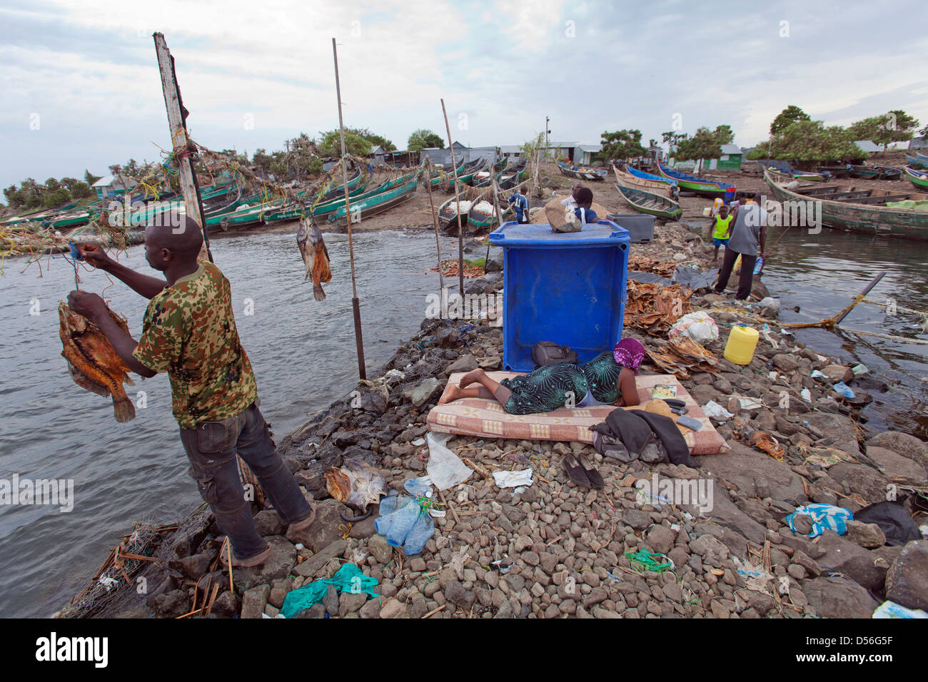 Uomo di essiccazione di persico del Nilo per l' esportazione e la donna posa sul materasso in attesa per le barche per tornare, Remba Island, il lago Victoria, in Kenya. Foto Stock