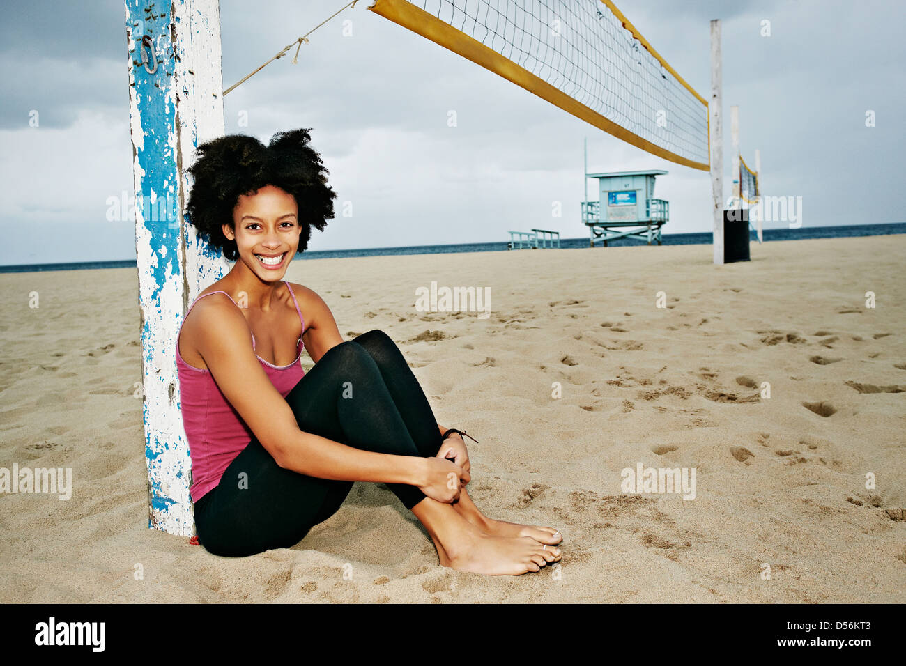 Razza mista donna seduta dalla rete da pallavolo sulla spiaggia Foto Stock