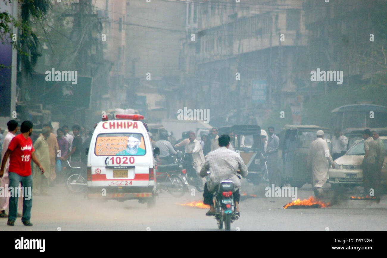 Pendolari passano in prossimità bruciando pneumatici che sono istoriati da manifestanti arrabbiati durante la manifestazione di protesta dei residenti di Kharadar contro il funzionamento mirato dai rangers funzionari, in area torre a Karachi. Foto Stock