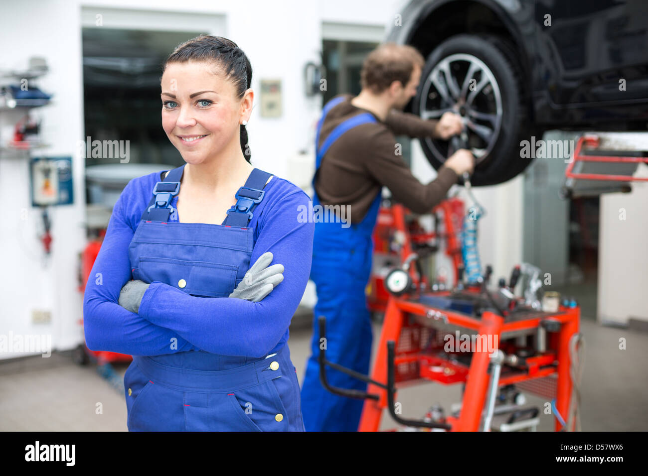 Meccanico femmina in piedi in officina, un altro meccanico cambia una ruota ad un auto su un sollevatore idraulico Foto Stock