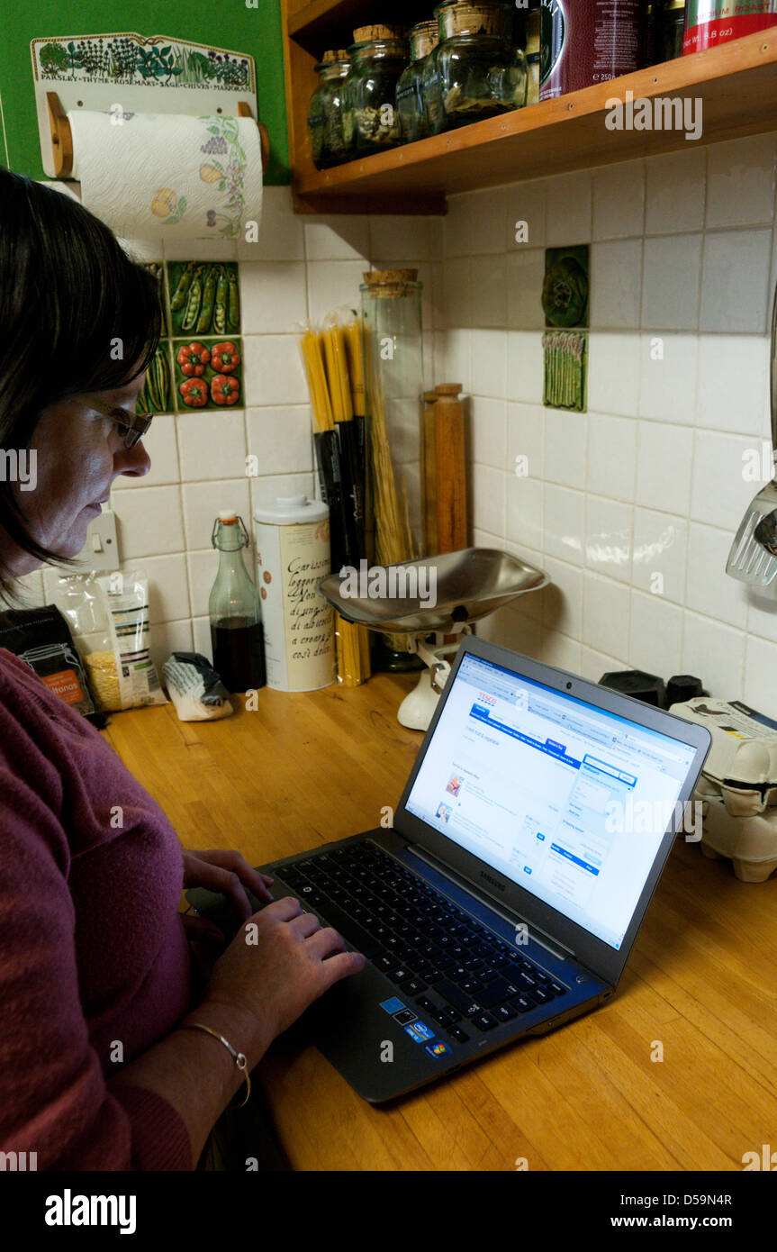 Una donna che utilizza un computer portatile nella sua cucina per ordinare del cibo dal sito web di un supermercato online. Foto Stock