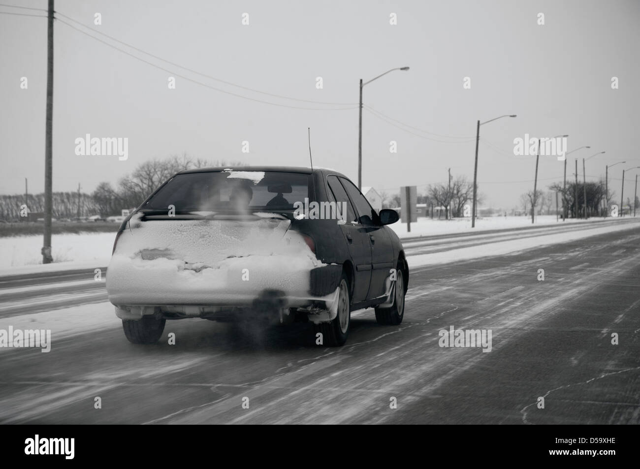 Retro della vettura viene intonacata con neve su una autostrada vuota con lavori di soffiaggio della neve nelle zone rurali del Canada Foto Stock