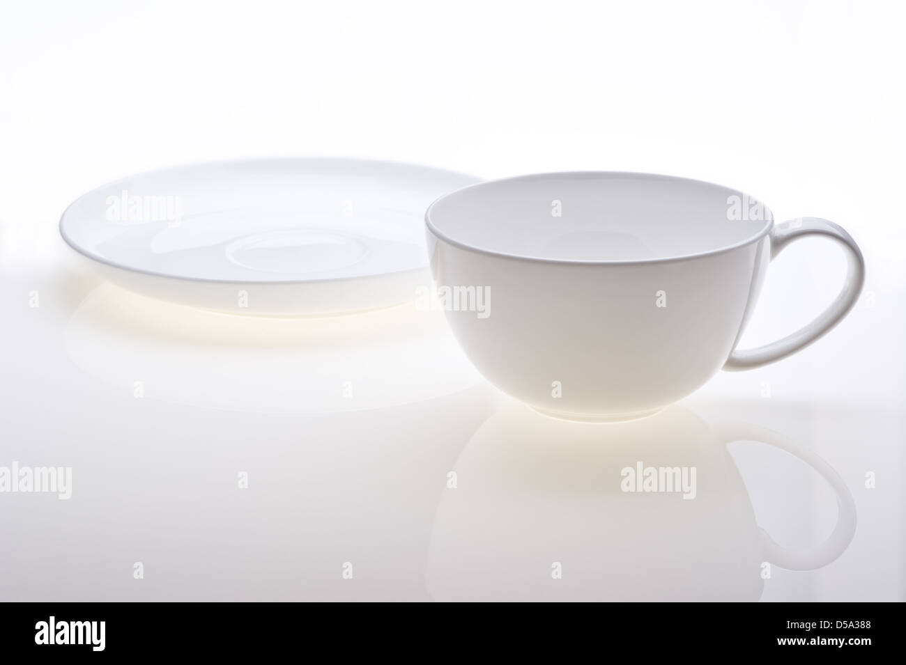 Tazza e piattino in piedi separatamente su sfondo bianco. Con riflessioni in primo piano. Foto Stock