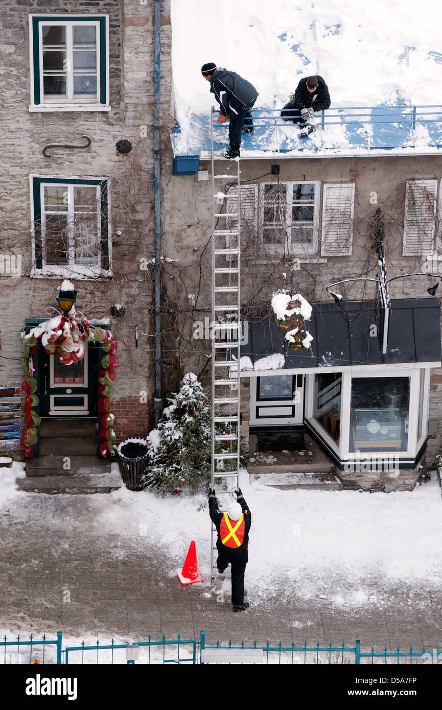 Un lavoratore detiene una scaletta per i colleghi la scalata verso il basso dopo spalare la neve fuori da un tetto nella Vecchia Quebec, Canada. Foto Stock