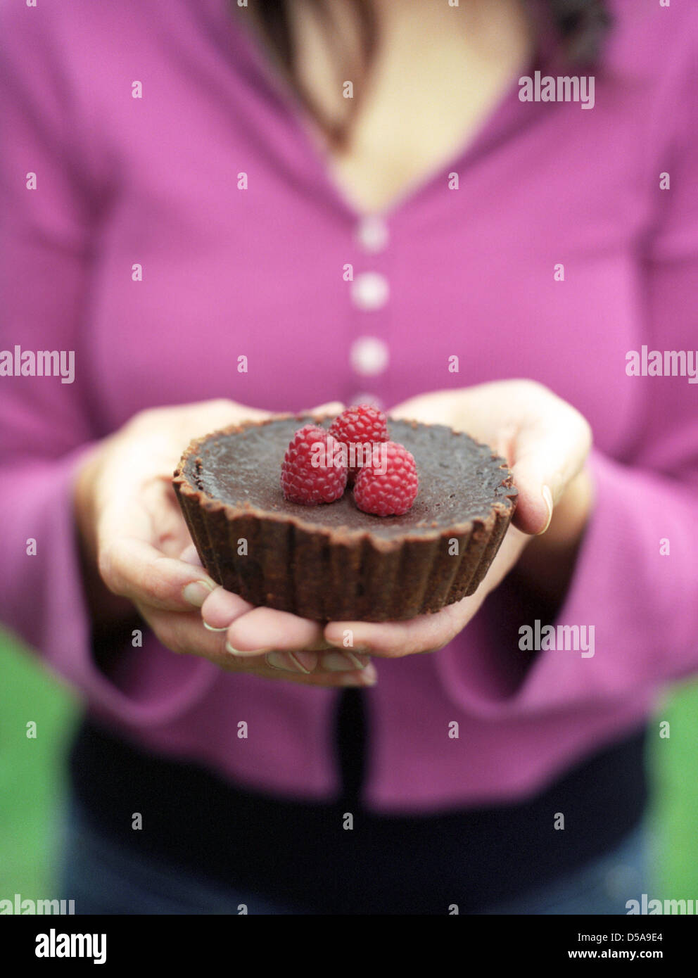 Una torta al cioccolato e rabboccato con lamponi è tenuto in mano da una giovane donna verso il visualizzatore. Foto Stock