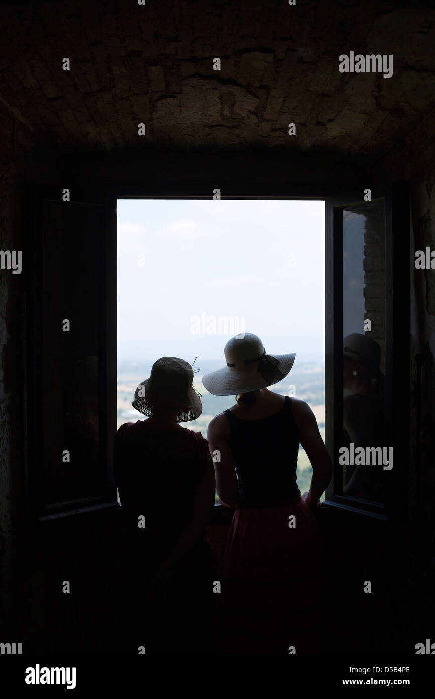 Due donne stagliano guardando fuori attraverso una finestra su una valle Toscana Foto Stock