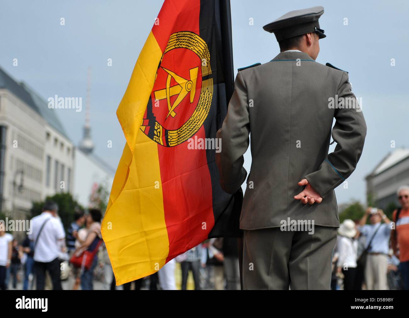 Un uomo rivestita di un Oriente esercito tedesco pone uniforme con una bandiera della RDT sulla Pariser Platz davanti alla Porta di Brandeburgo a Berlino, Germania, 13 agosto 2010. Scattare foto con le bandiere della RDT e memorabilia di GDR è popolare con i turisti di Berlino. Il 13 agosto 1961, la costruzione del muro di Berlino ha cominciato a Berlino Est. Foto: RAINER JENSEN Foto Stock