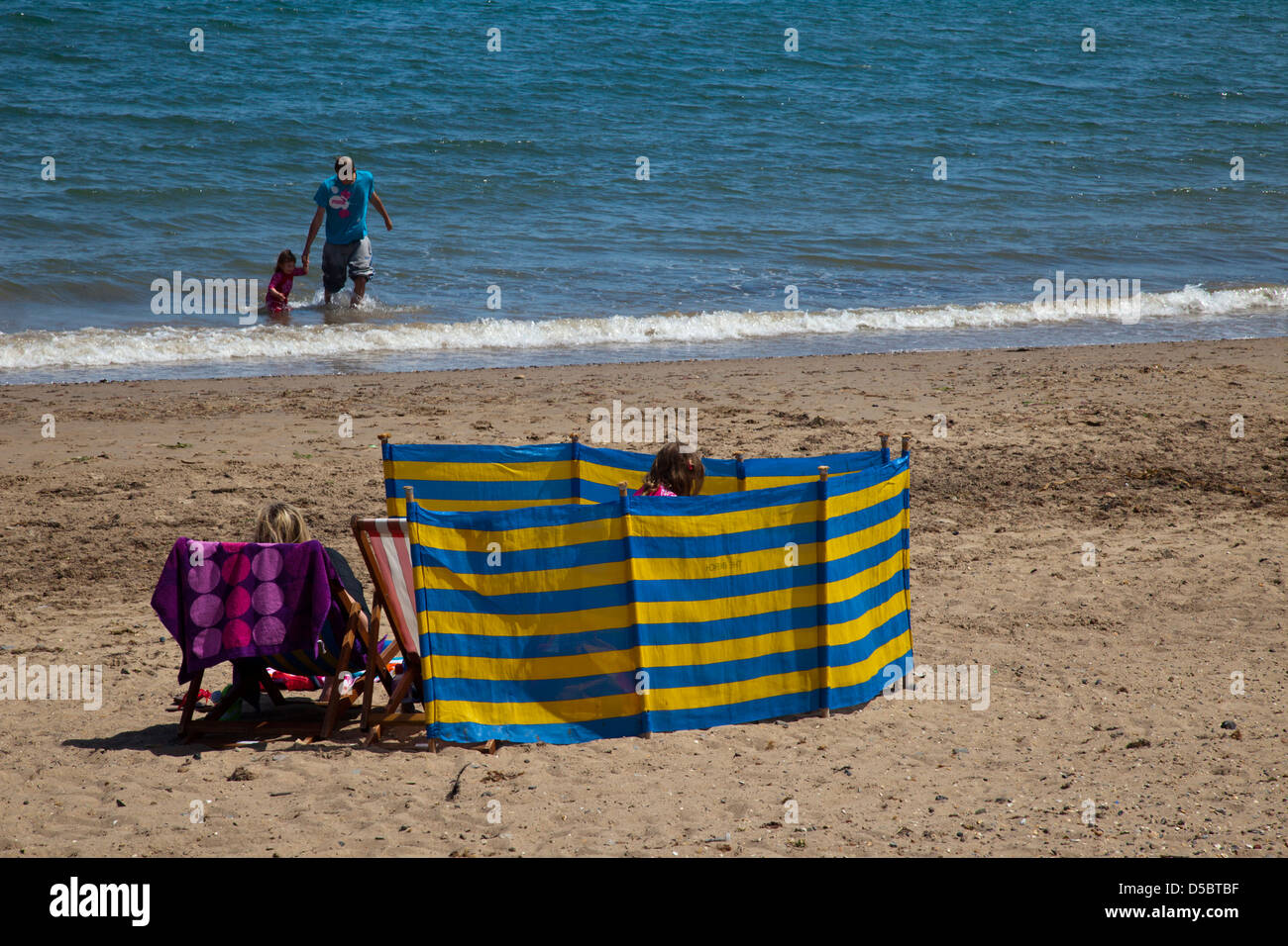 Una famiglia rifugiandosi dietro un frangivento a Swanage beach in Dorset England Regno Unito Foto Stock