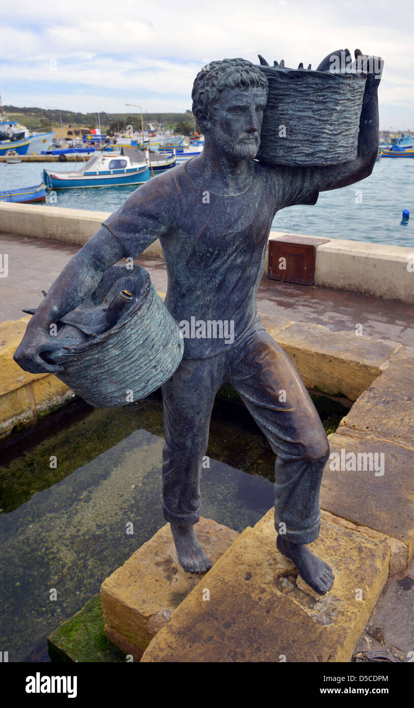 Statua di bronzo di pescatore presso il porto e la Baia di Marsaxlokk, Malta. Foto Stock