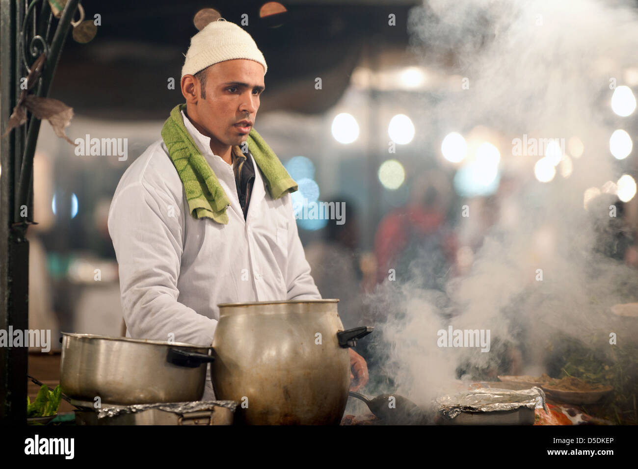 Un uomo la cottura su una smokey incendio di un cibo locale di stallo nel mercato Djemaa al fna in Marrkesh, Marocco Foto Stock