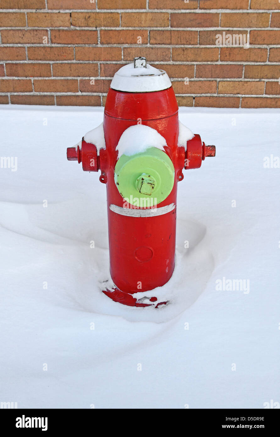 Rosso fuoco idrante coperte da neve, in prossimità di un edificio in mattoni. Foto Stock