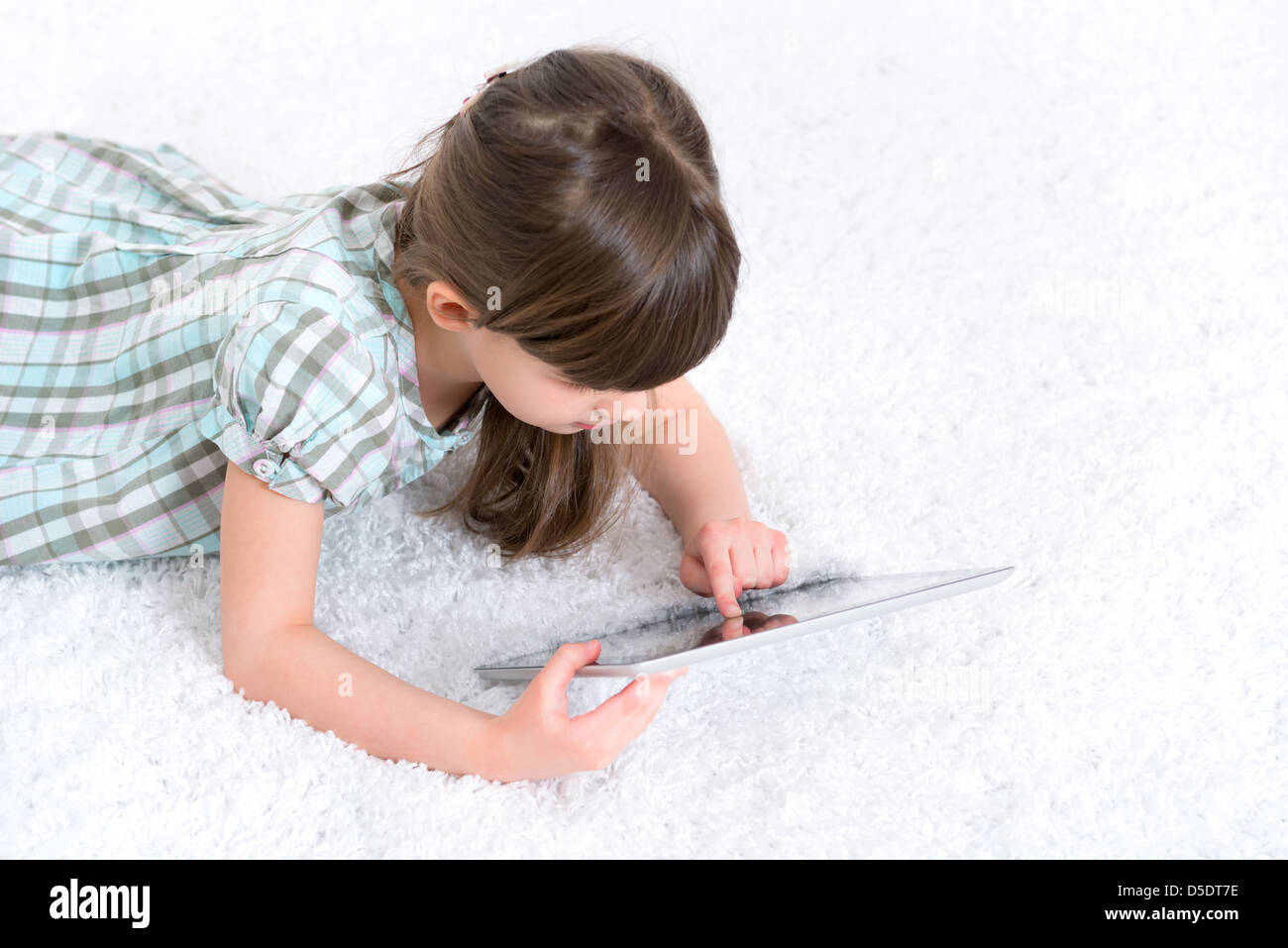 Ragazza giovane (6-7 anno) guardando e giocando con tavoletta digitale in una camera bianca. Foto Stock