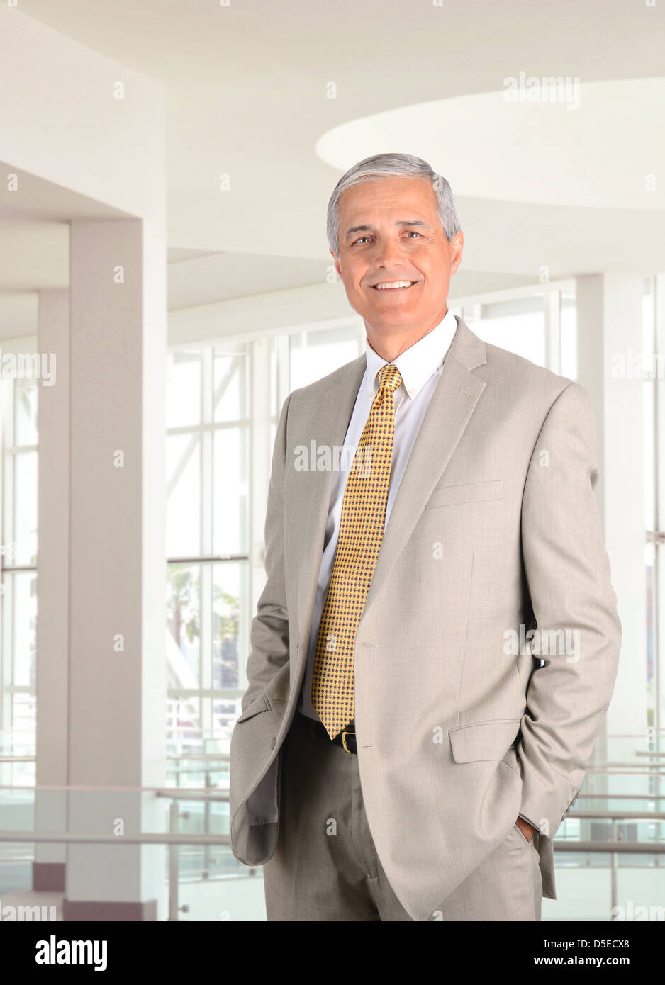 Primo piano di un medio imprenditore invecchiato in piedi in un ufficio moderno impostazione con le mani nelle tasche dei pantaloni. Formato verticale. Foto Stock