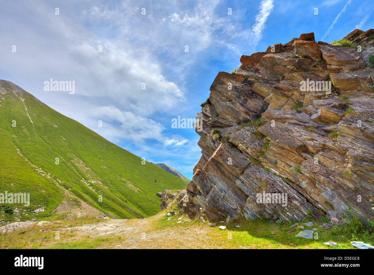Verdi pendii alpini e formazioni rocciose sotto il bellissimo cielo al Colle delle Finestre passano nelle Alpi italiane. Foto Stock