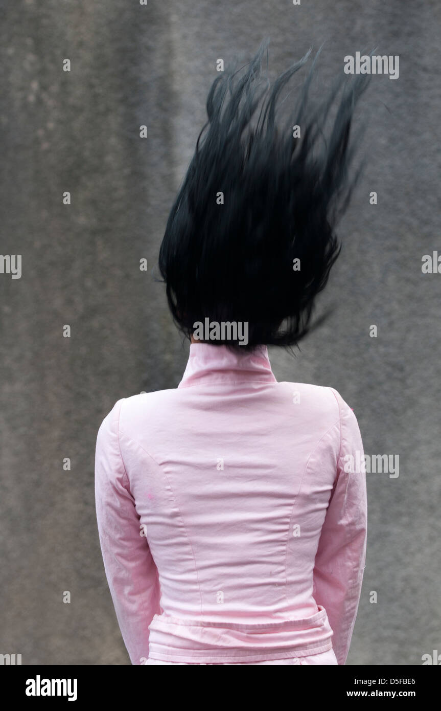 Vista posteriore di una giovane donna in camicia rosa sfogliare i suoi capelli Foto Stock