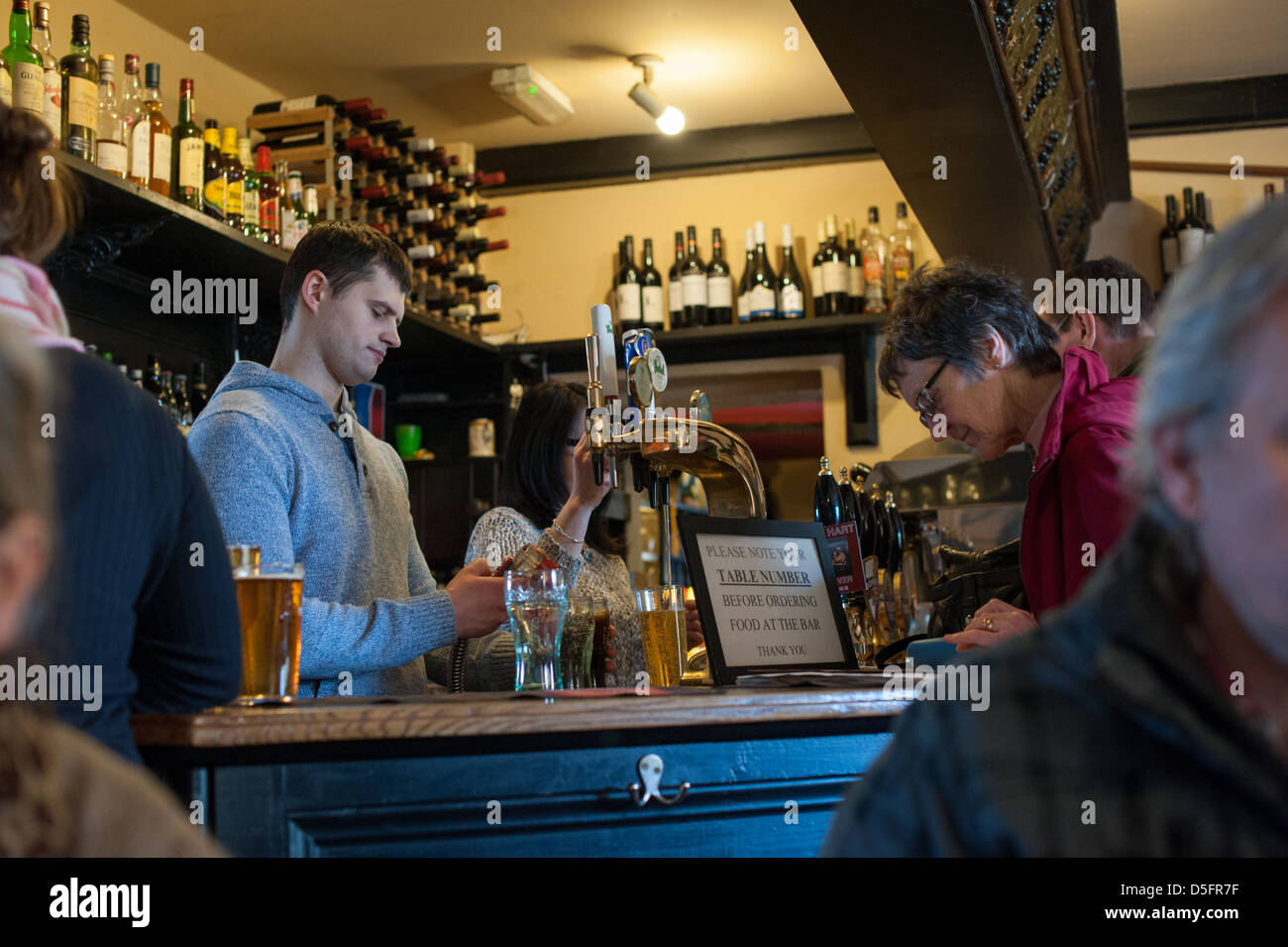 Bianco giovane uomo bar che serve birra a una donna più anziana in un paese di lingua inglese pub su un inverno la giornata con un drink al bar Foto Stock