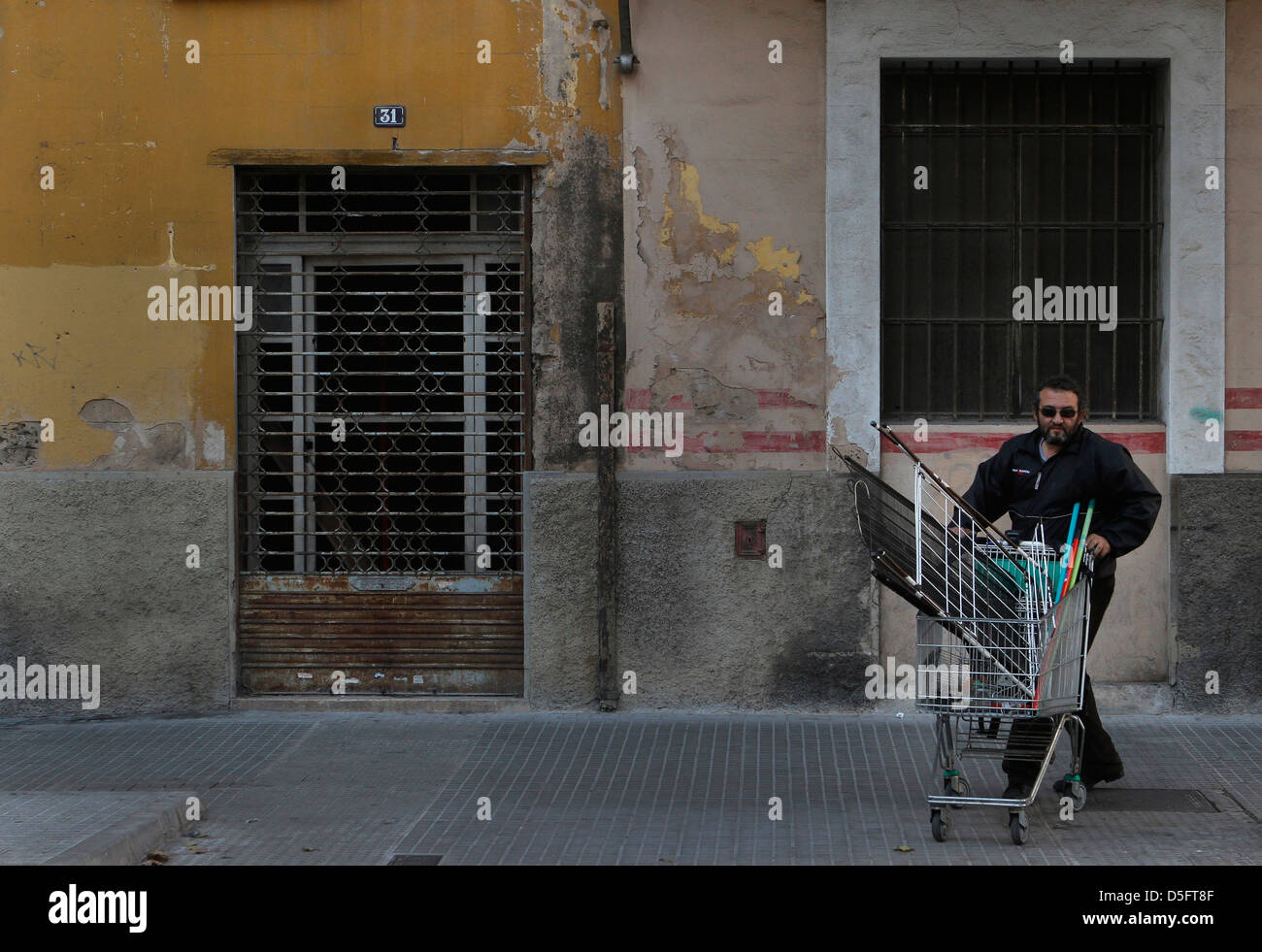 Un disoccupato uomo tira un carrello per trasportare la posta indesiderata trovati sui contenitori. Foto Stock