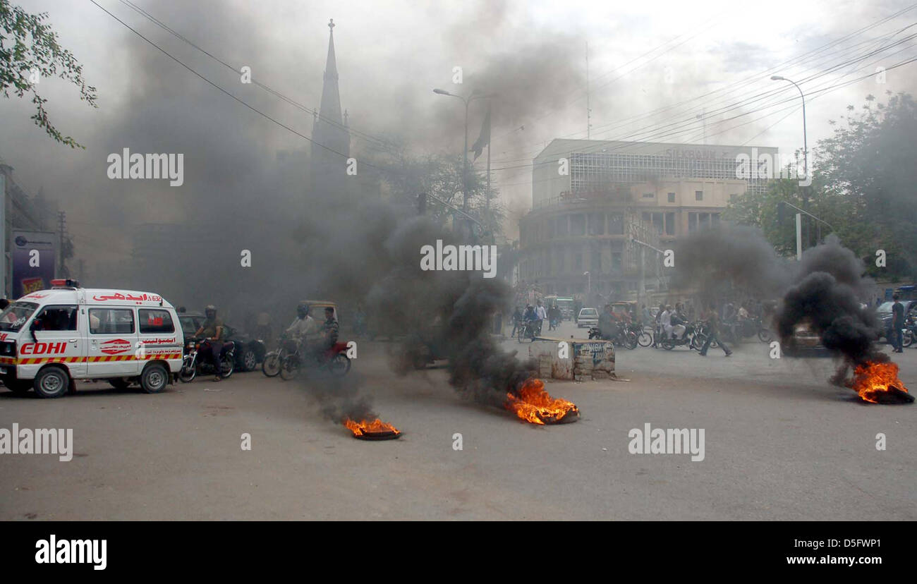 Pendolari passano in prossimità bruciando pneumatici che sono istoriati da manifestanti arrabbiati durante la manifestazione di protesta dei residenti di Kharadar contro il funzionamento mirato dai rangers funzionari, in area torre a Karachi. Foto Stock