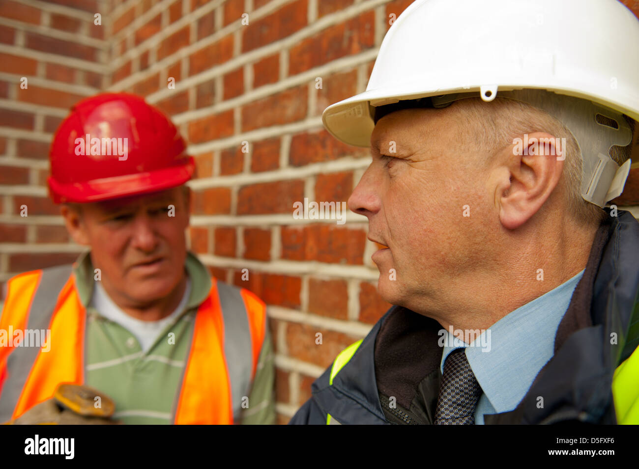 Workman e sito in costruzione foreman parlare contro un muro di mattoni in background. Foto Stock