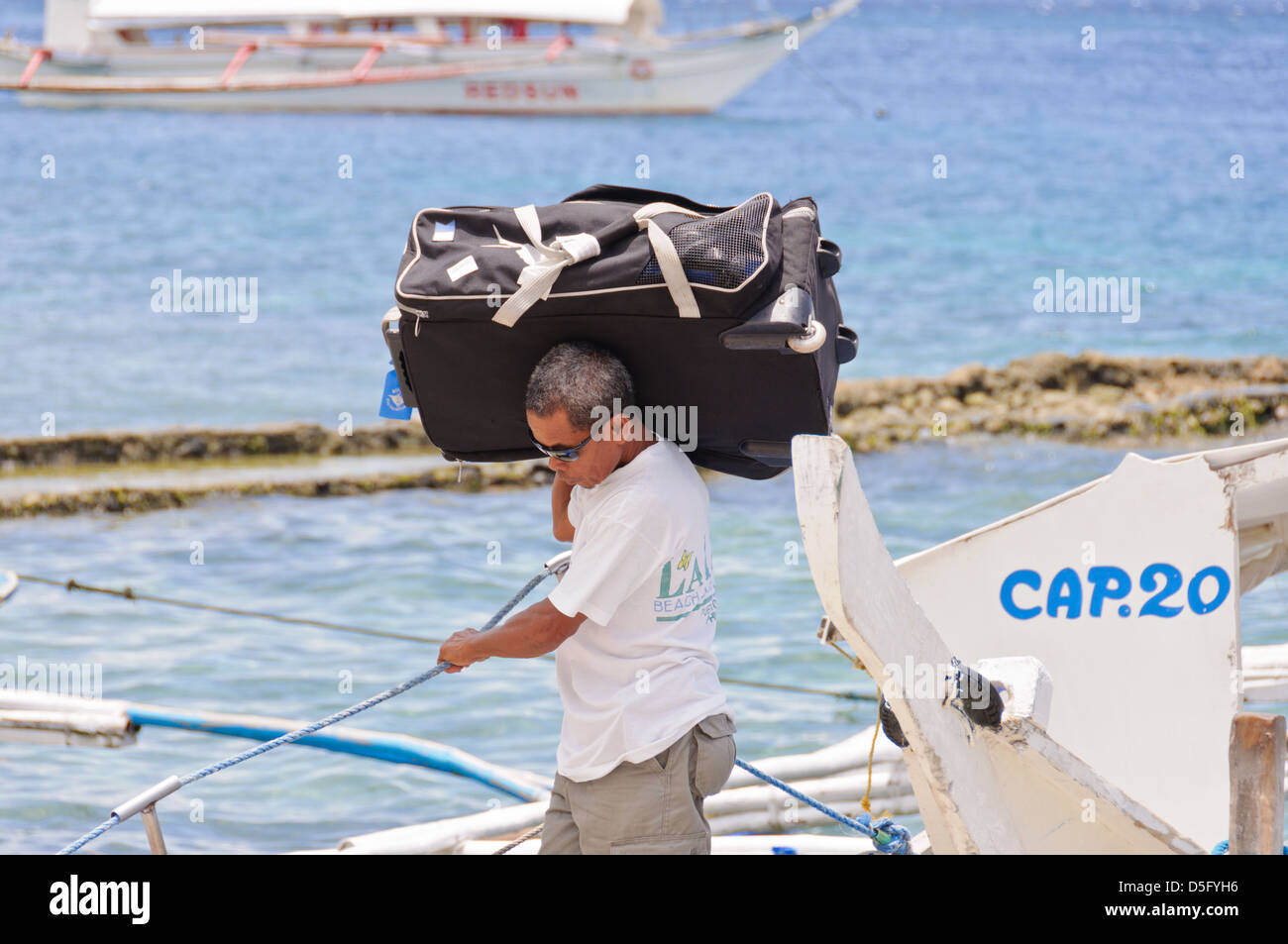 Maschio portiere asiatico porta grande bagaglio pesante da un piccolo traghetto passeggeri barca - Sabang, Puerto Galera, Filippine, Asia Foto Stock
