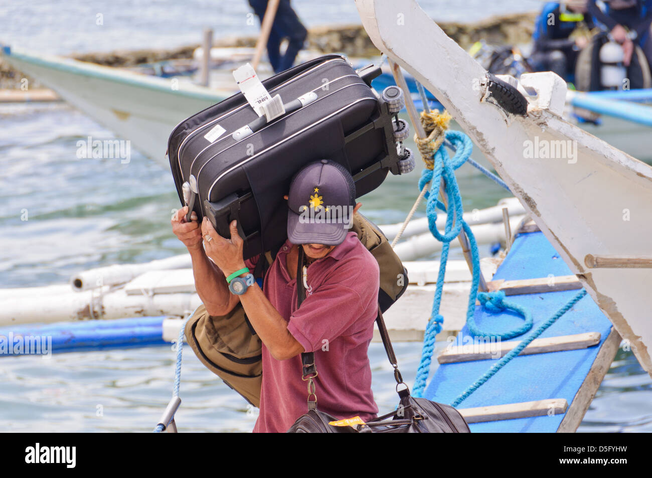 Maschio portiere asiatico porta grande bagaglio pesante da un piccolo traghetto passeggeri barca - Sabang, Puerto Galera, Filippine, Asia Foto Stock