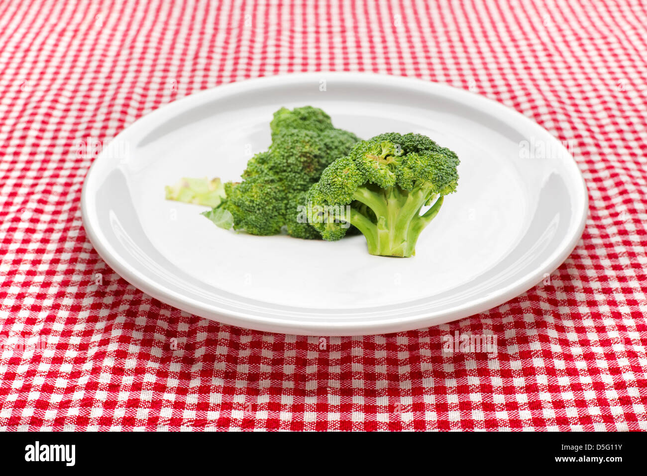 Crudo fresco broccoli su una piastra bianca.Il bianco e il rosso a scacchi tovaglia cucina in background. Foto Stock