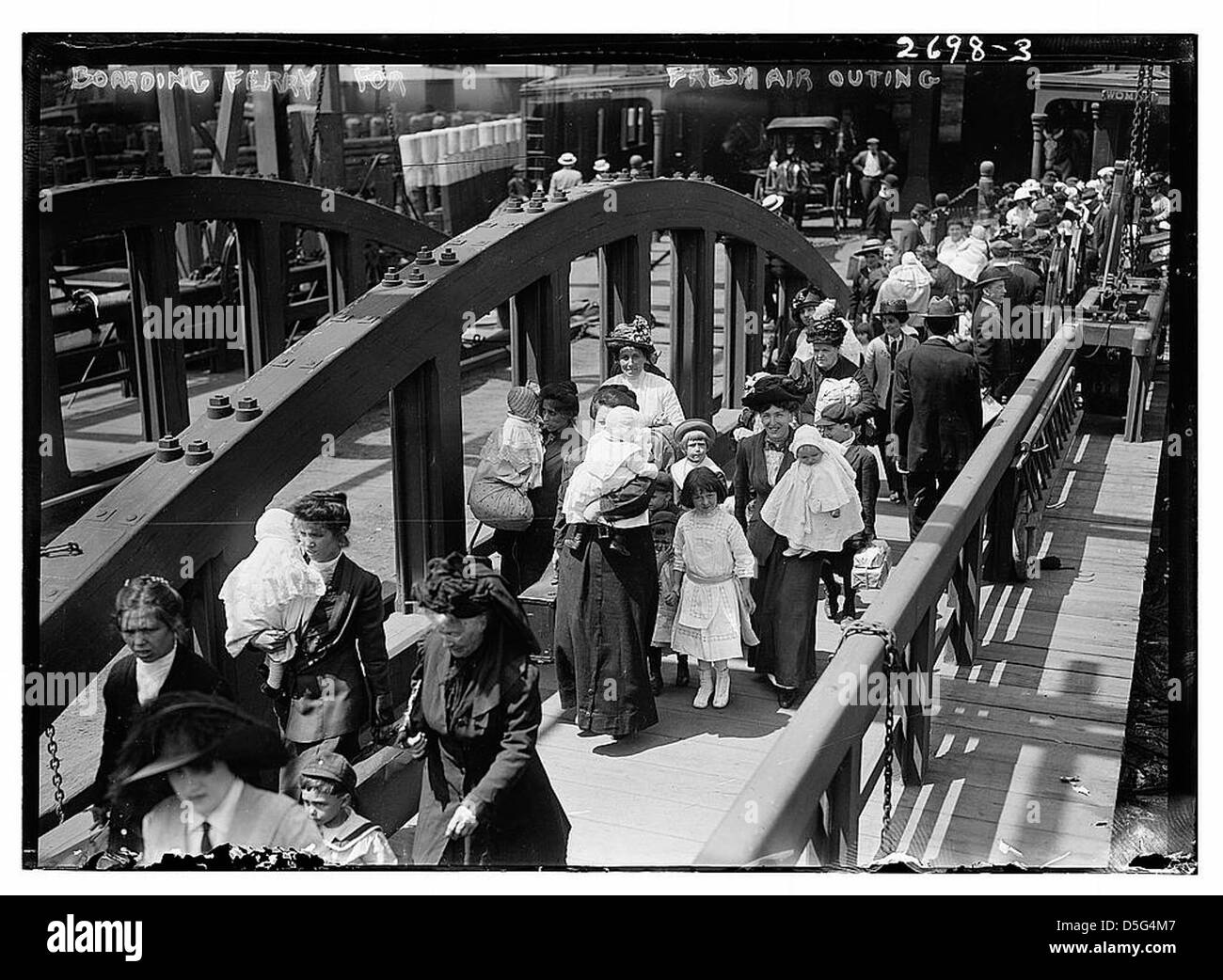 Questa fotografia cattura i bambini che salgono su un traghetto per una gita all'aria aperta nel 1913. Scattata il 2 giugno, l'immagine mostra una folla in attesa di imbarcarsi al molo, con molti cappelli. Riflette gli sforzi caritatevoli dell'epoca per fornire escursioni all'aria aperta ai bambini, una pratica comune per i bambini della città all'inizio del XX secolo. Foto Stock