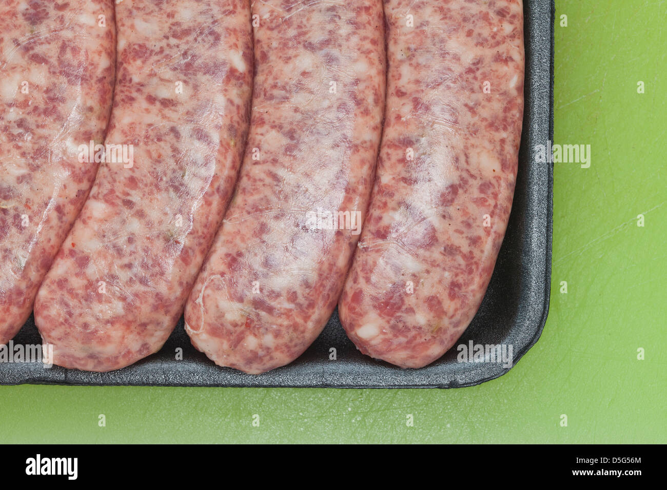 Carne cruda salsiccia, brat,in plastica nera su sfondo verde, Foto Stock