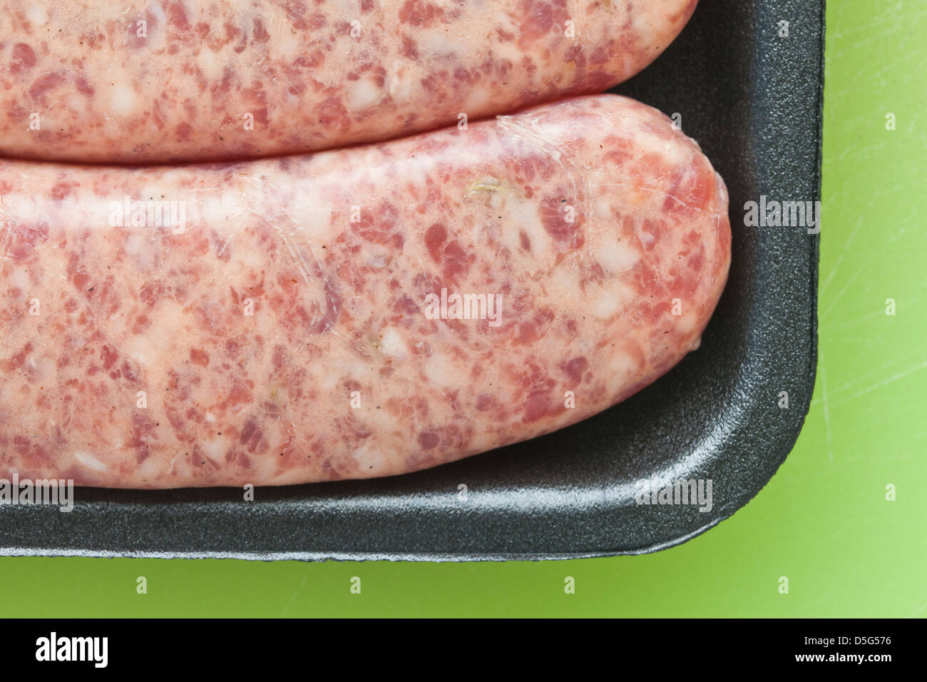 Carne cruda salsiccia, brat,in plastica nera su sfondo verde, Foto Stock
