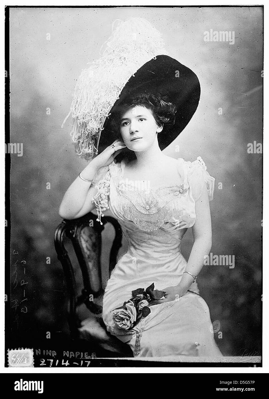 L'attrice Nina Napier è mostrata in un ritratto glamour, seduta su una sedia. È vestita con un abito alla moda e un grande cappello con piume, che incarna gli standard di moda e bellezza dell'epoca. Foto Stock