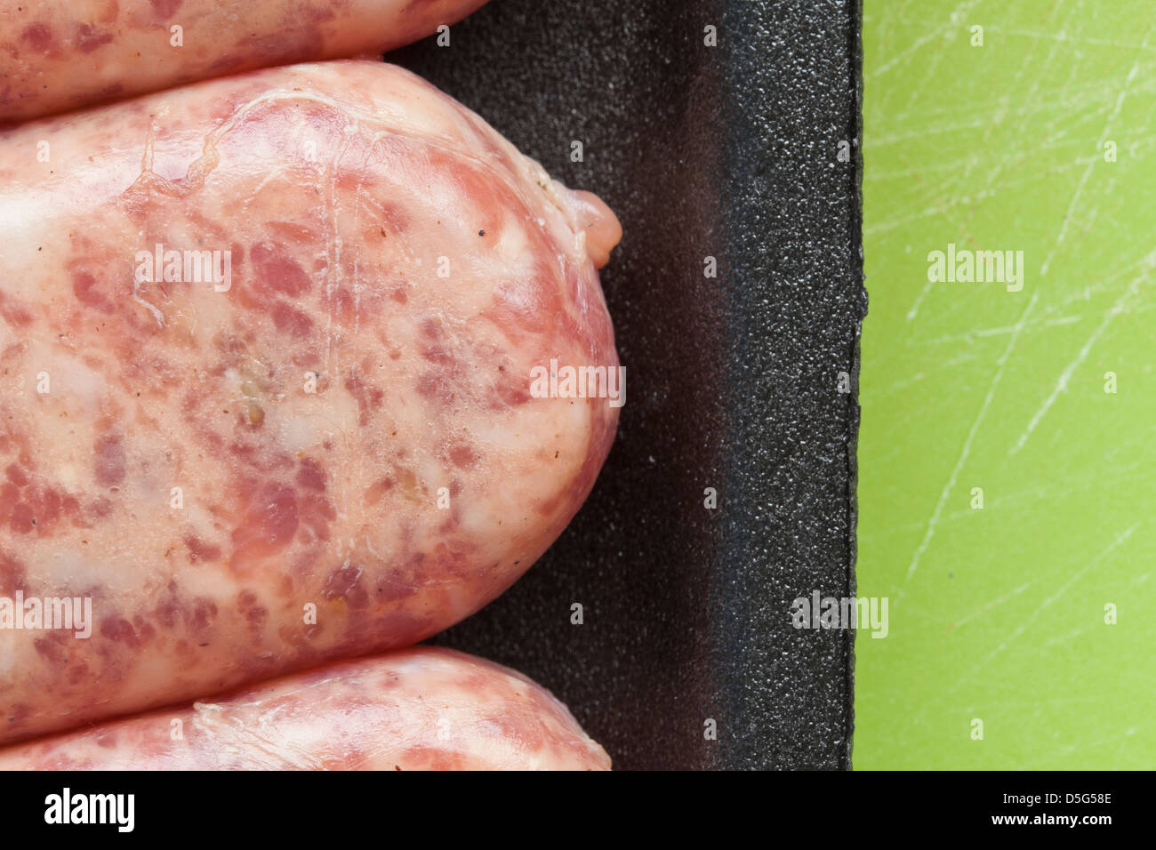 Carne cruda salsiccia, brat,in plastica nera su sfondo verde, Foto Stock