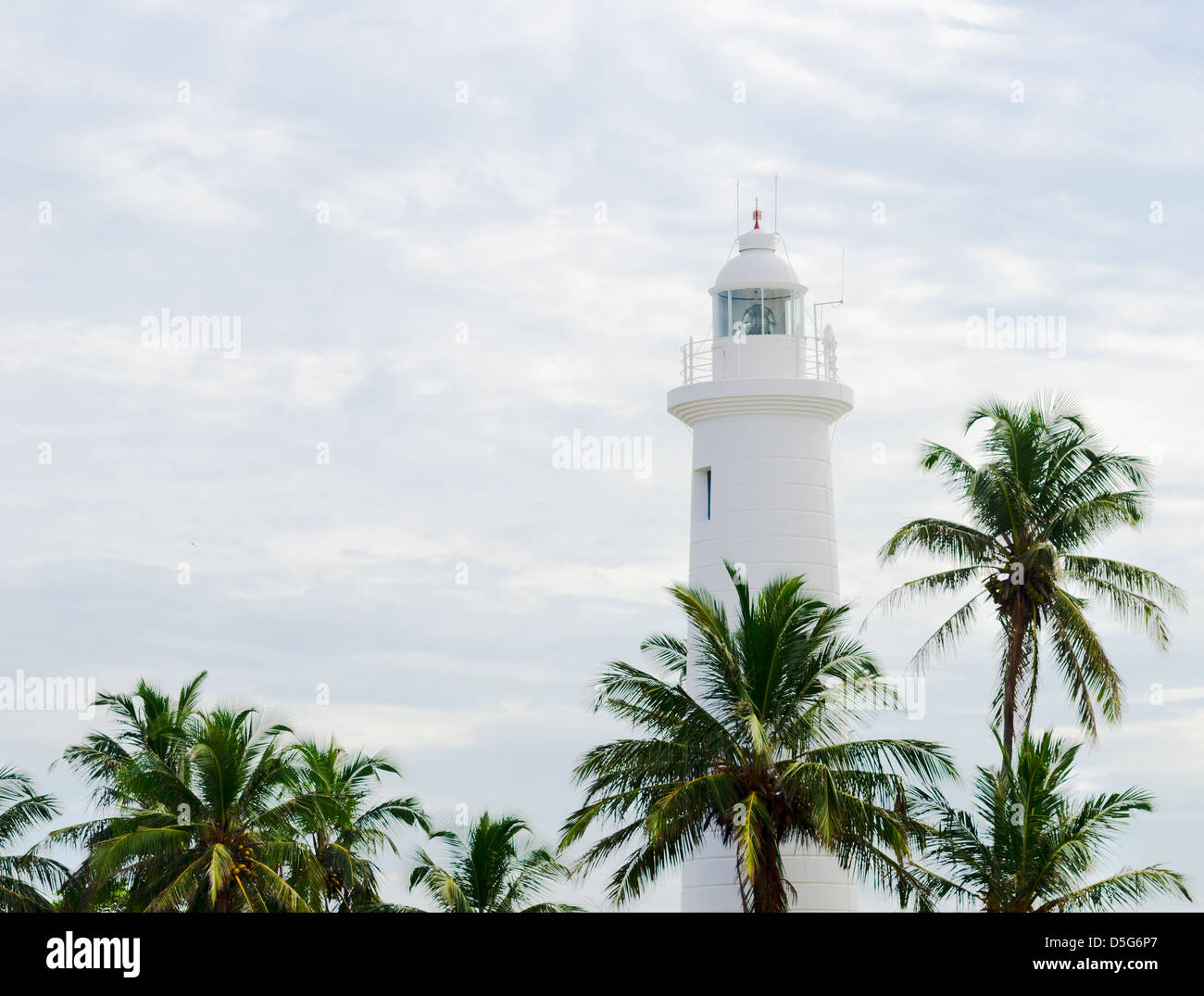 Faro di colore bianco al di sopra di palm tops su sfondo con cielo nuvoloso, Galle Sri Lanka Foto Stock