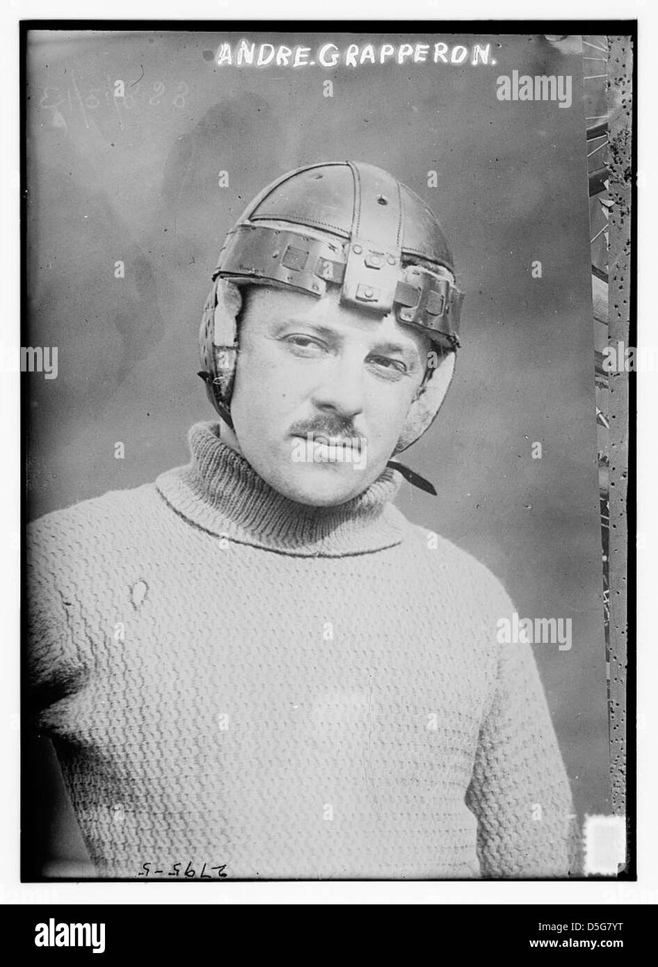 Un ritratto di Andre Grapperon, un pilota francese che indossa un casco e un maglione. Grapperon viene catturato in una classica posa da corsa, mostrando i suoi baffi distintivi. L'immagine riflette la cultura delle prime corse motociclistiche in Francia, evidenziando la crescente popolarità di questo sport durante l'inizio del XX secolo. Foto Stock