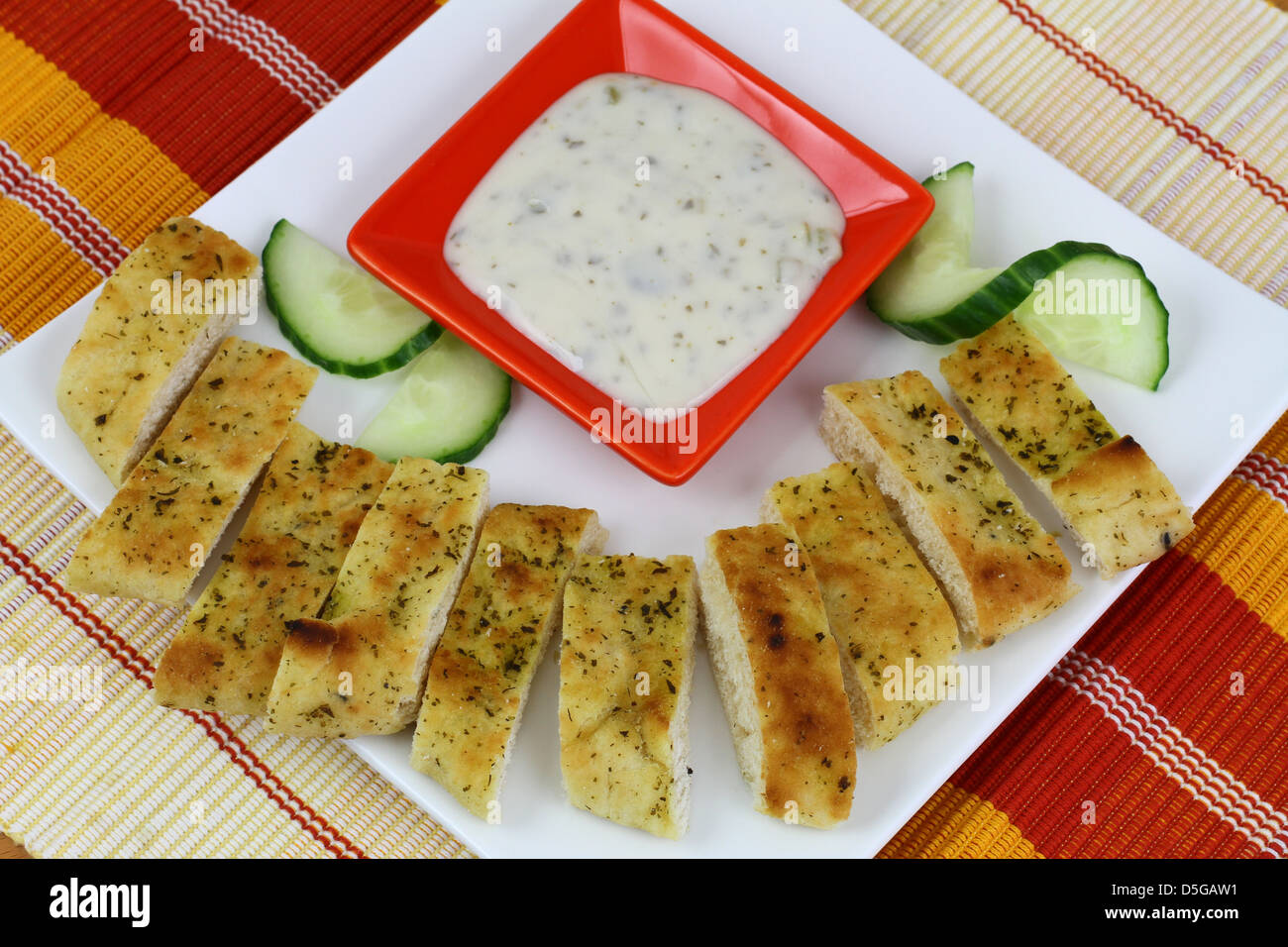 Nan pezzi di pane con raita di cetriolo su piastra bianca Foto Stock