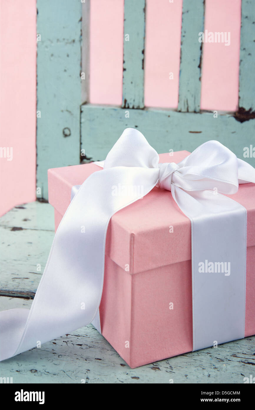 Romantica rosa confezione regalo con il bianco satin su una luce blu sedia in legno Foto Stock