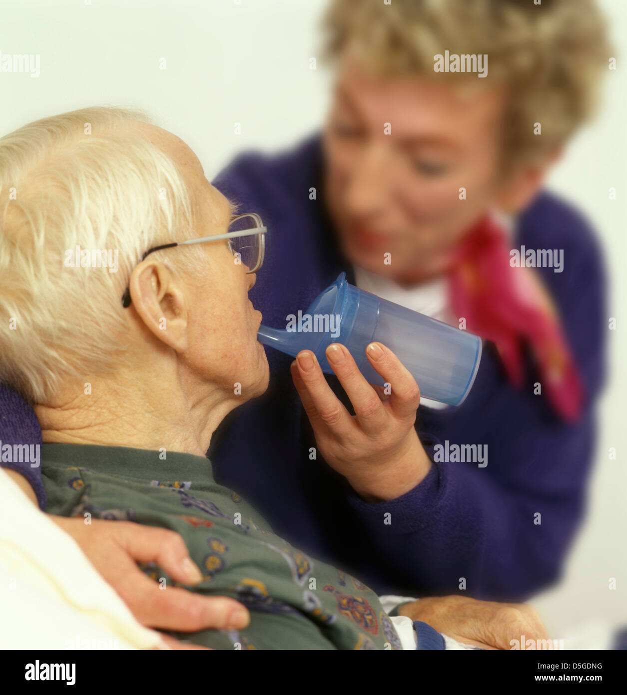 Il caregiver informale di alimentazione di un vecchio in bisogno di cure uomo con un alimentatore di pap Foto Stock