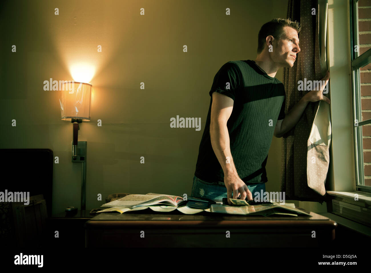 L'uomo a guardare fuori dalla finestra accanto alla scrivania Foto Stock