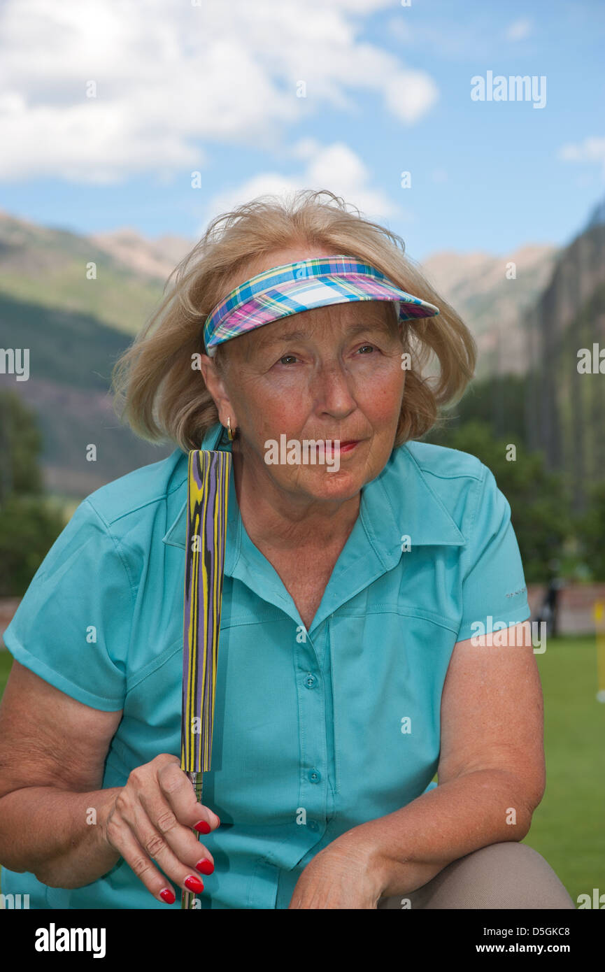Una femmina senior citizen si inclina verso il basso sul putting green e giudica la distanza della sua golf putt. Foto Stock