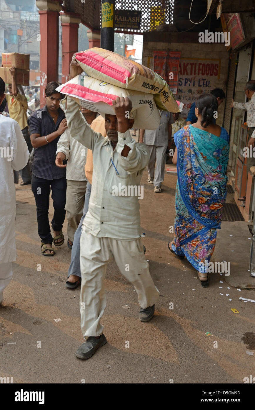 Un portatore che porta due sacchi di riso in testa in una strada trafficata, in Khari Baoli Road, Chandni Chowk, Old Delhi, India Foto Stock