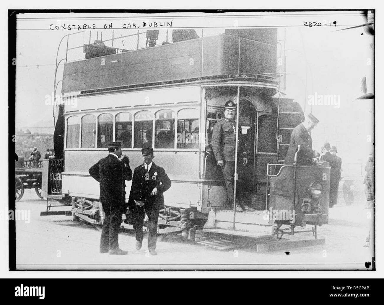 Questa fotografia mostra un agente su un'auto a Dublino, Irlanda, catturando la scena urbana della città con un autobus a due piani e un tram. Riflette il sistema dei trasporti pubblici e la polizia a Dublino, metà del XX secolo. Foto Stock