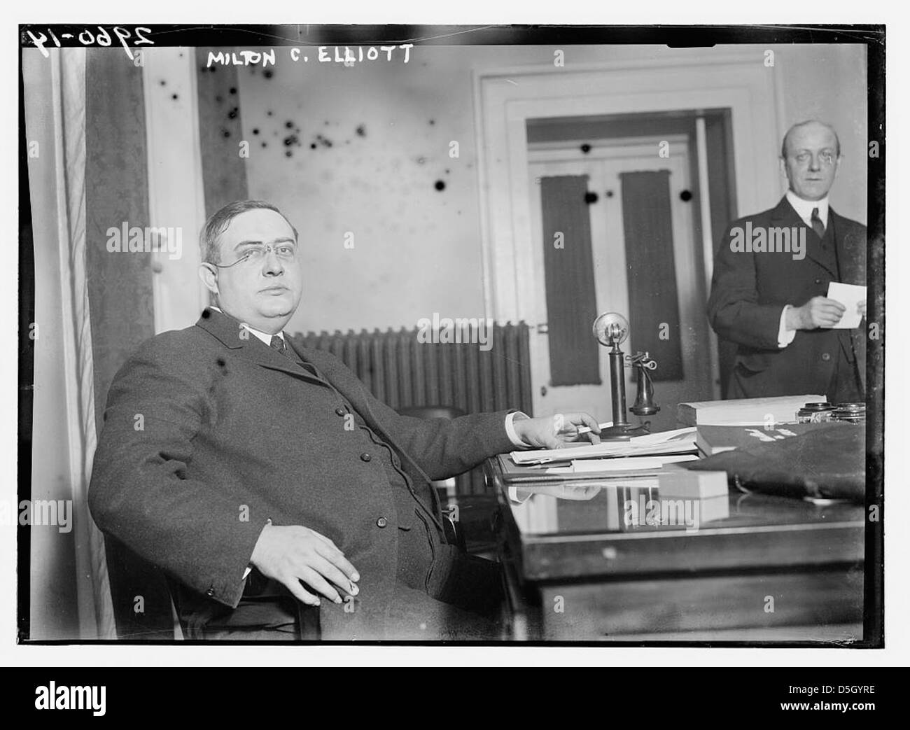 Milton C. Elliott, associato alla Federal Reserve, è visto seduto alla sua scrivania in una fotografia formale. Questa immagine lo cattura come una figura di spicco nella finanza americana. Foto Stock