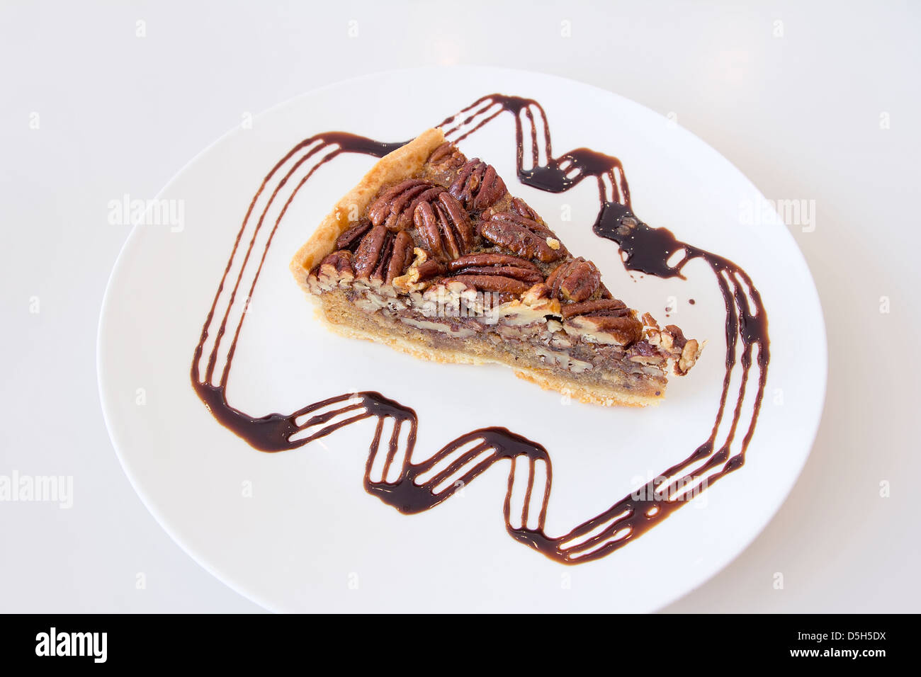 Noci Pecan torta con fetta con cioccolato fondente pioggerella su piastra bianca Foto Stock