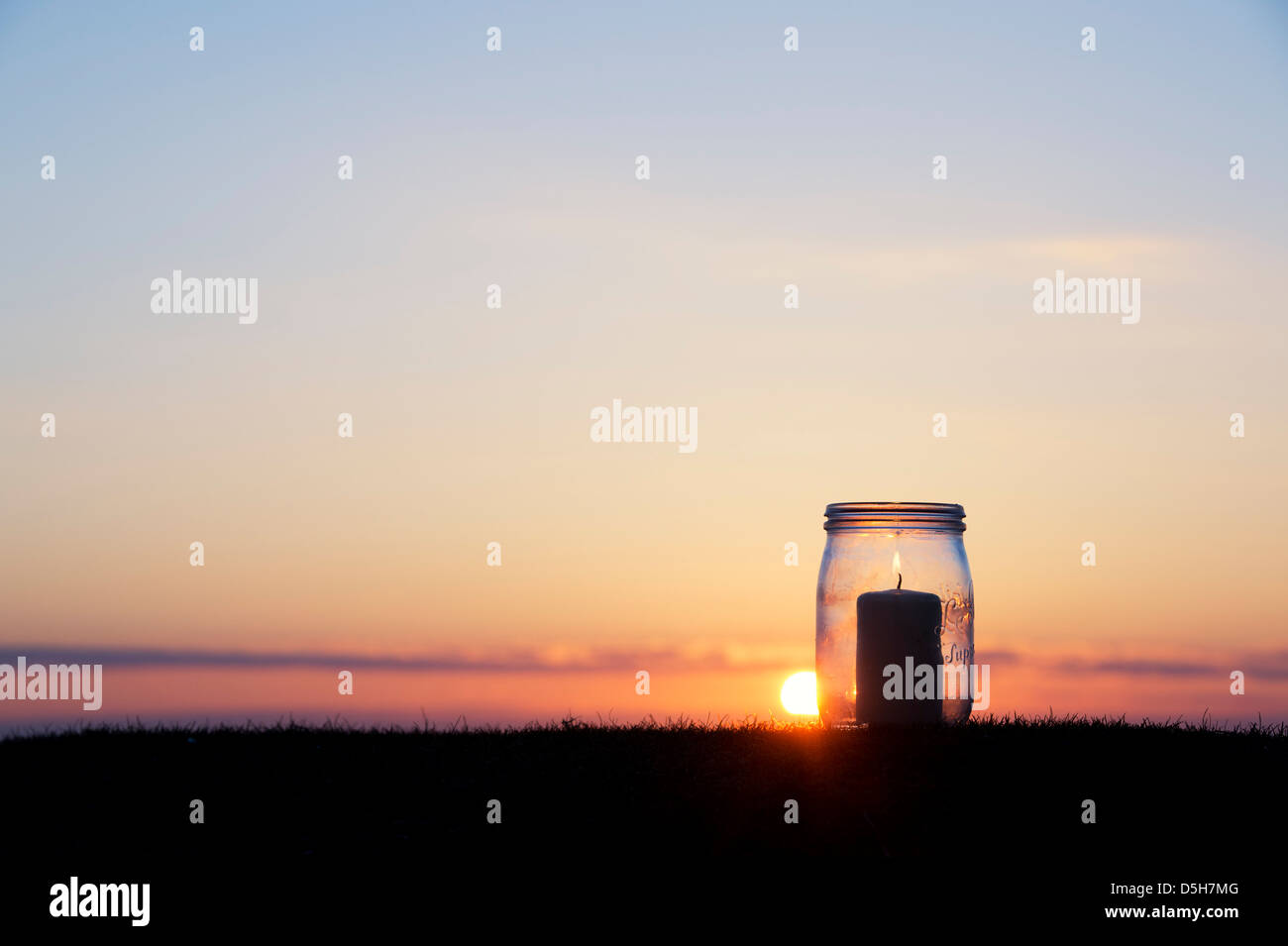 Candela in un barattolo di vetro a sunrise. Silhouette Foto Stock
